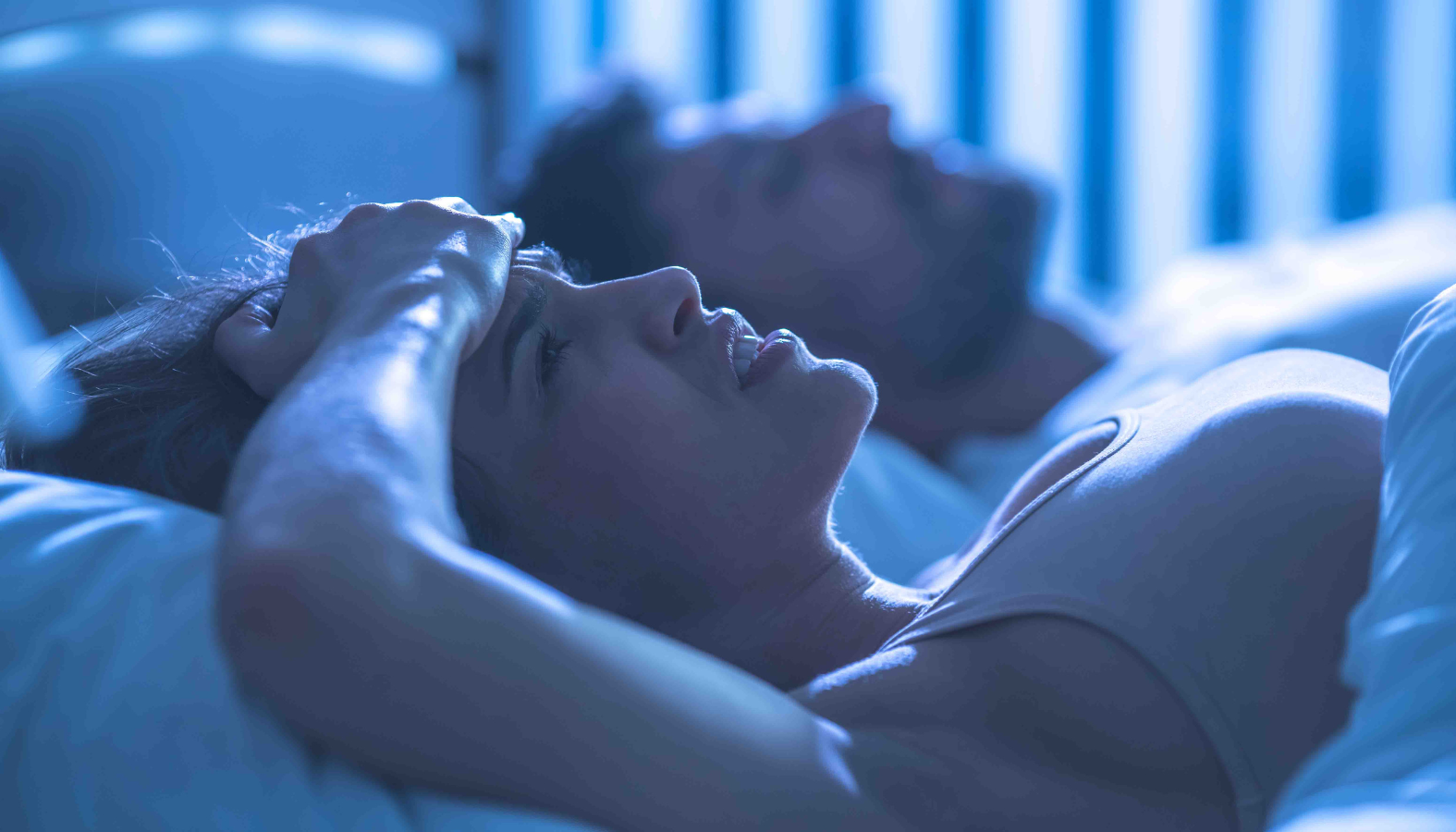 a woman lying in bed wide awake next to a man who is sleeping