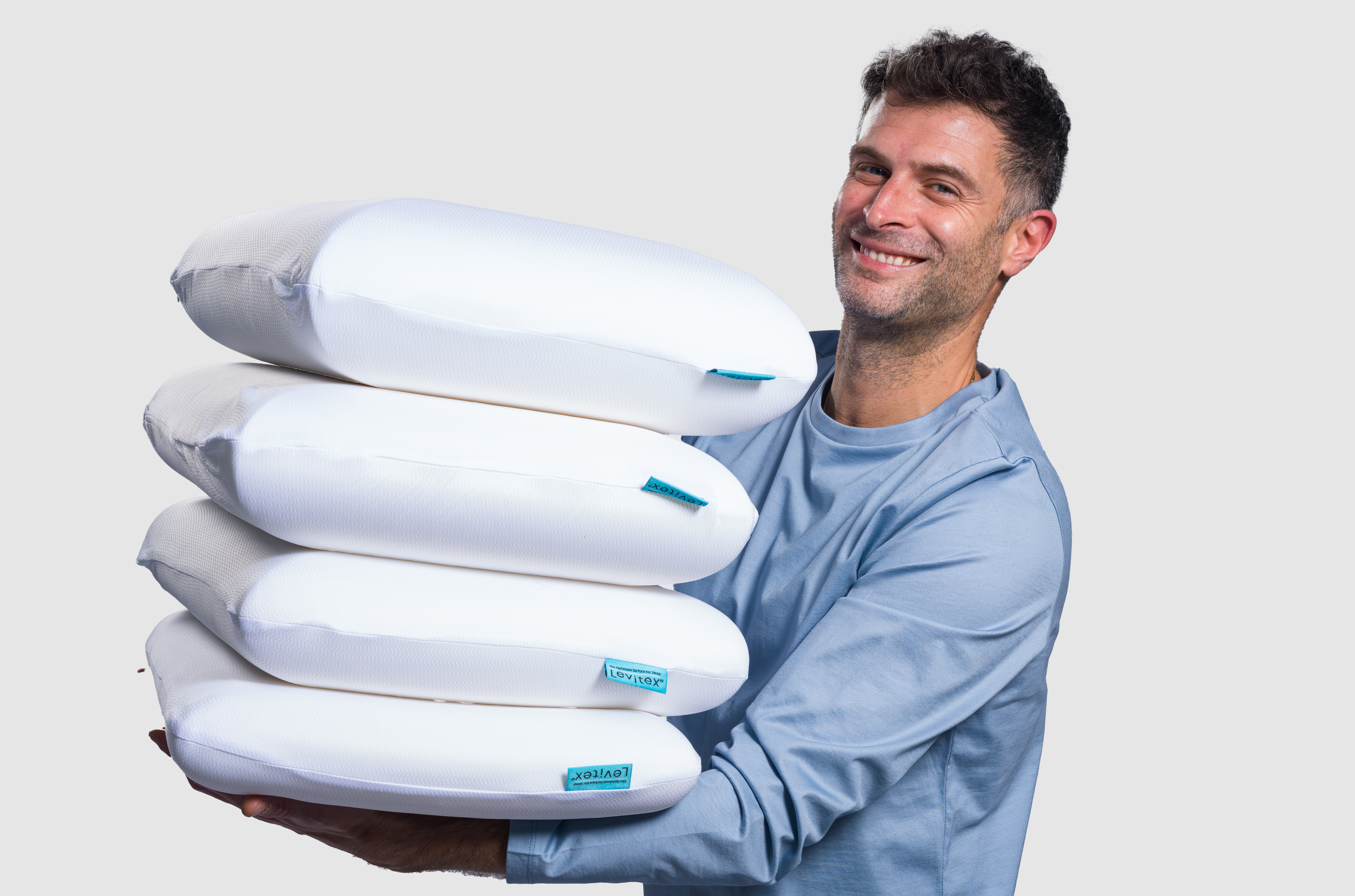 James Leinhardt holding multiple white pillows with a gray background