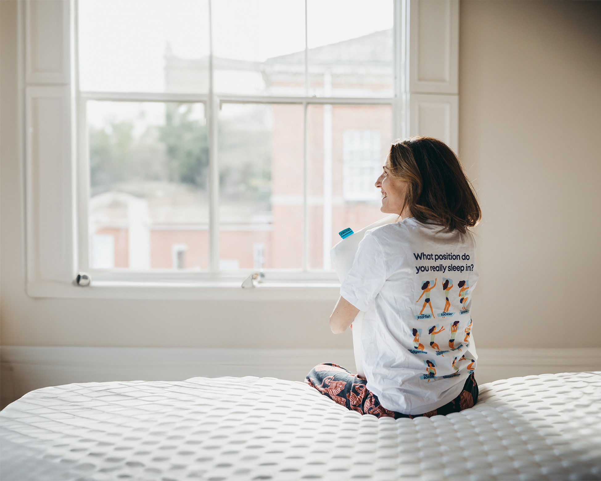 woman sitting on the edge of the bed holding a pillow in her arms