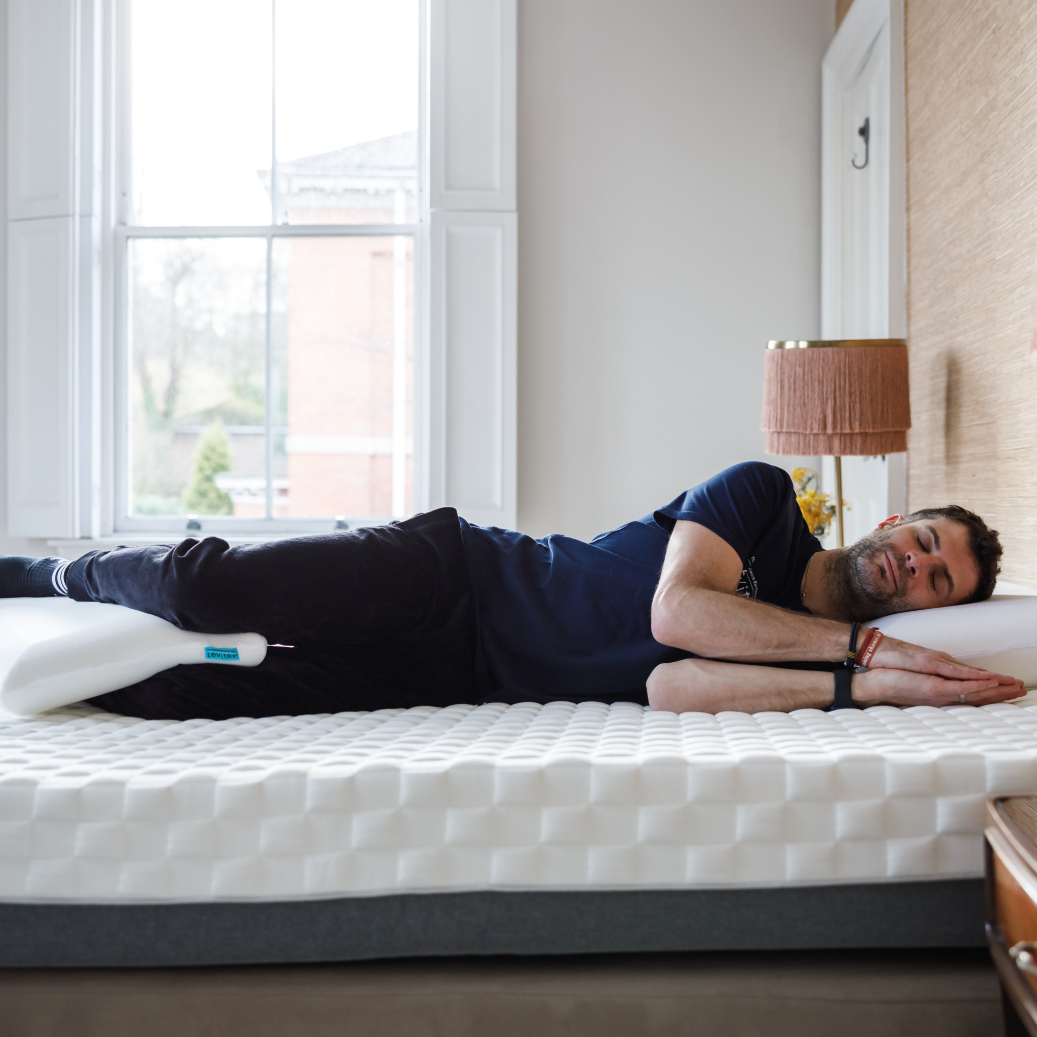 man lying on the bed in the dreamer position with pillow in between knees and ankles