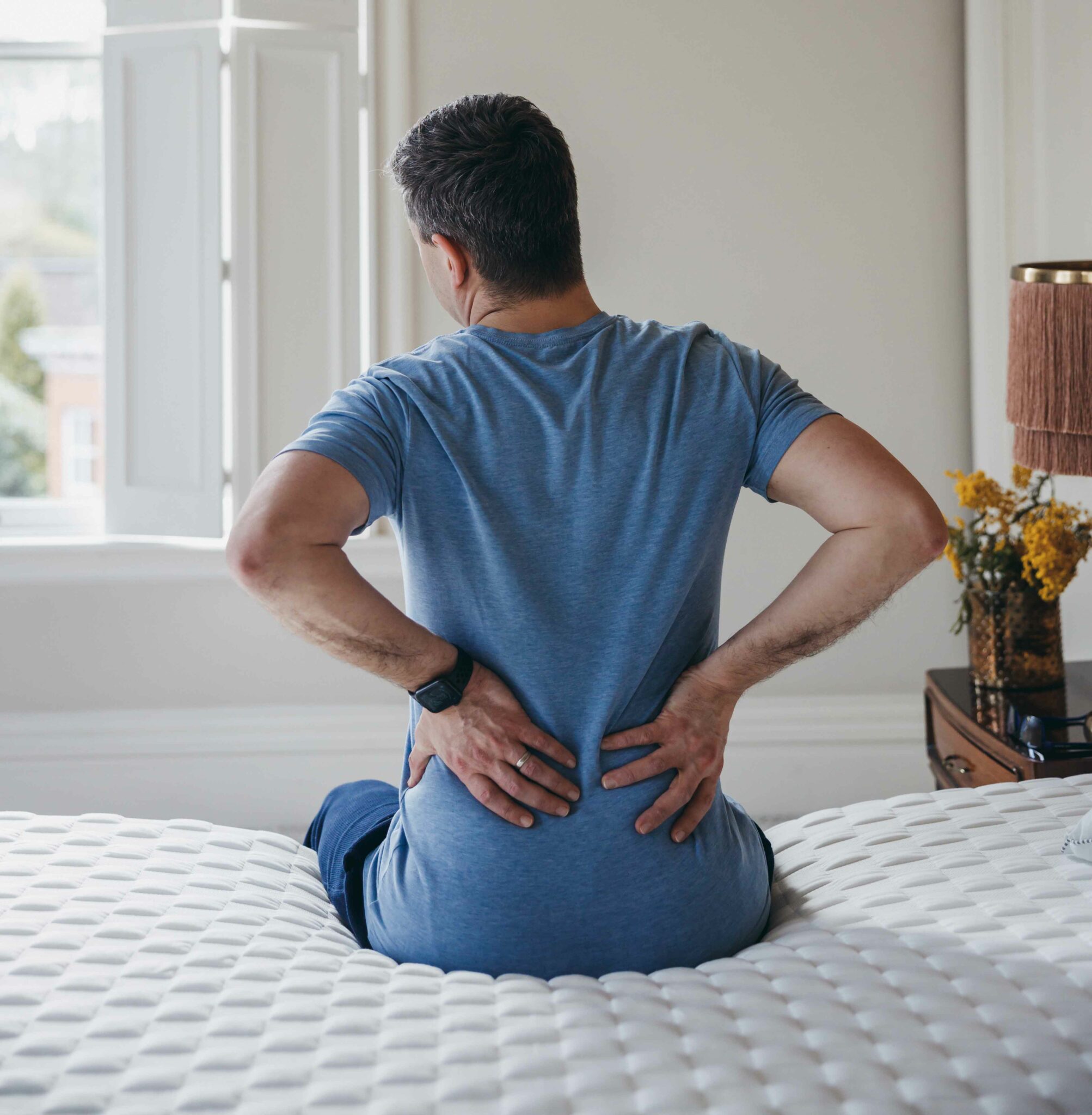 Man sitting on the bed in pain pressing his rubbing his lower back