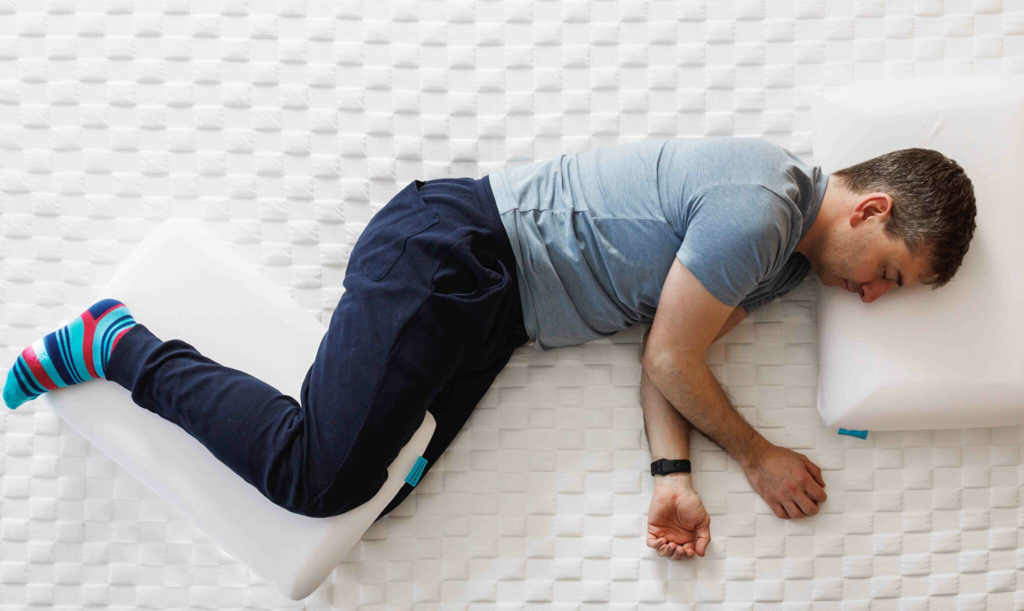 Man on a bed lying on his side with pillow in between his knees and ankles