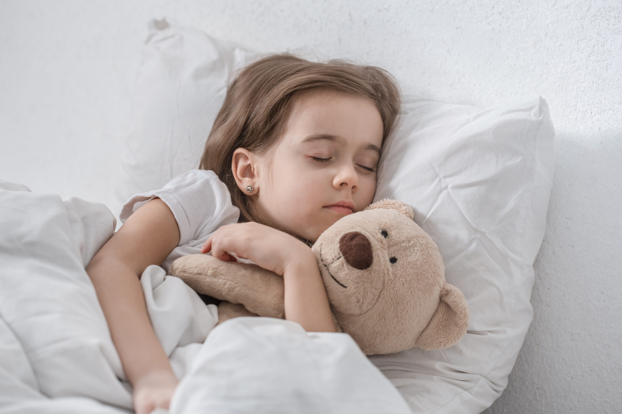 Little girl in a white bed sleeping with a soft toy