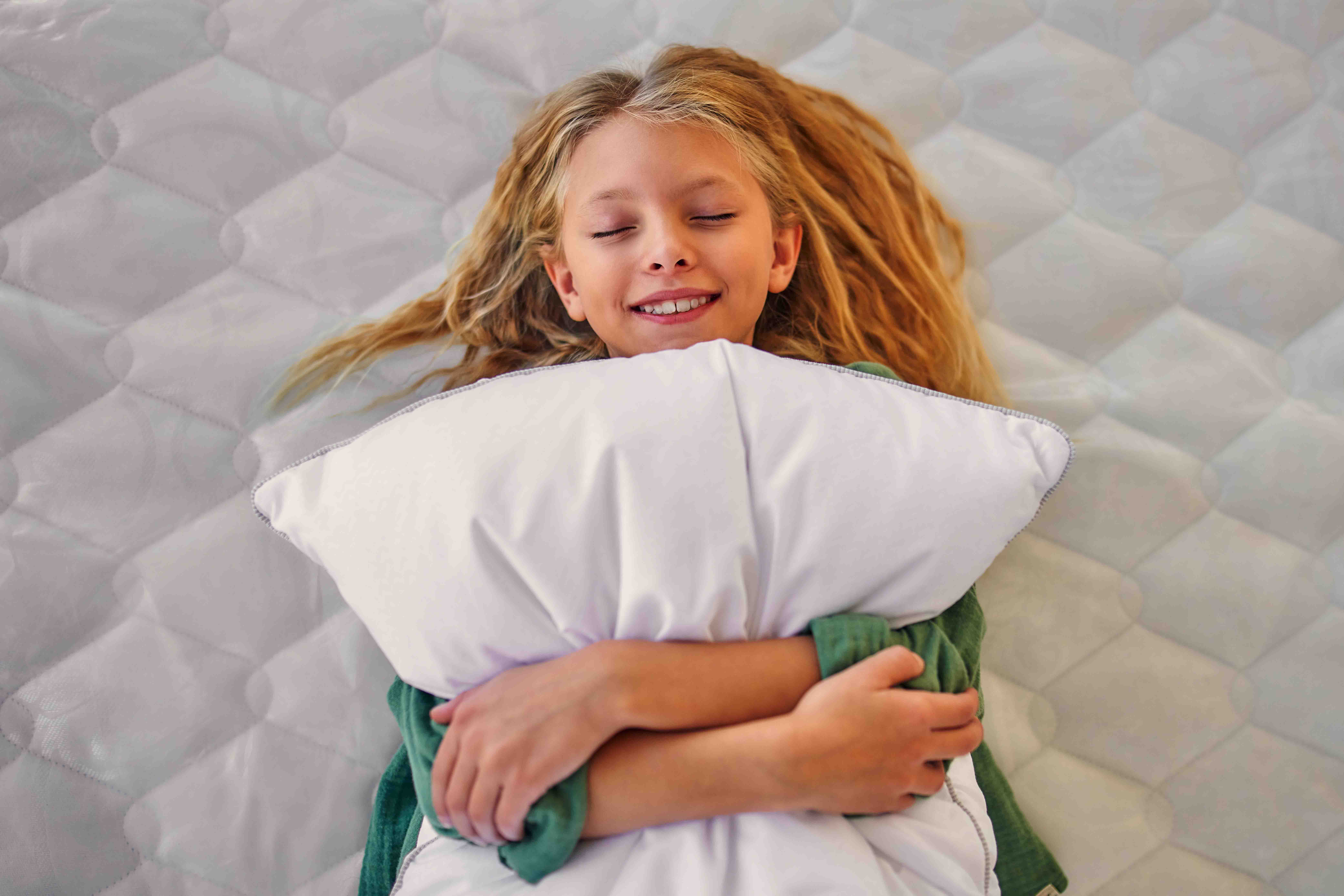 Girl lying on her back on a mattress clutching a pillow